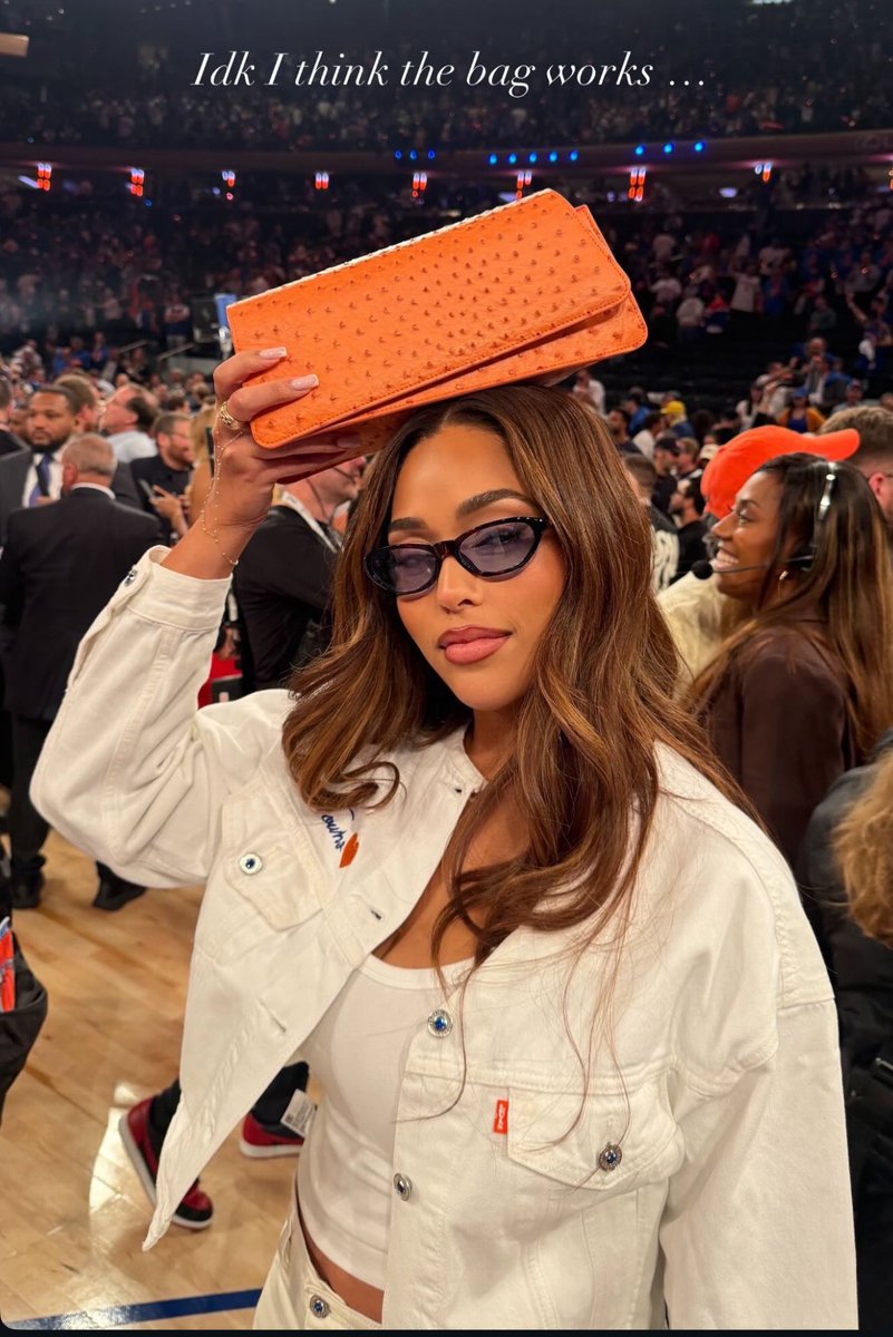 Jordyn Woods at Madison Square Garden holding her bright orange Woods by Jordyn clutch above her head