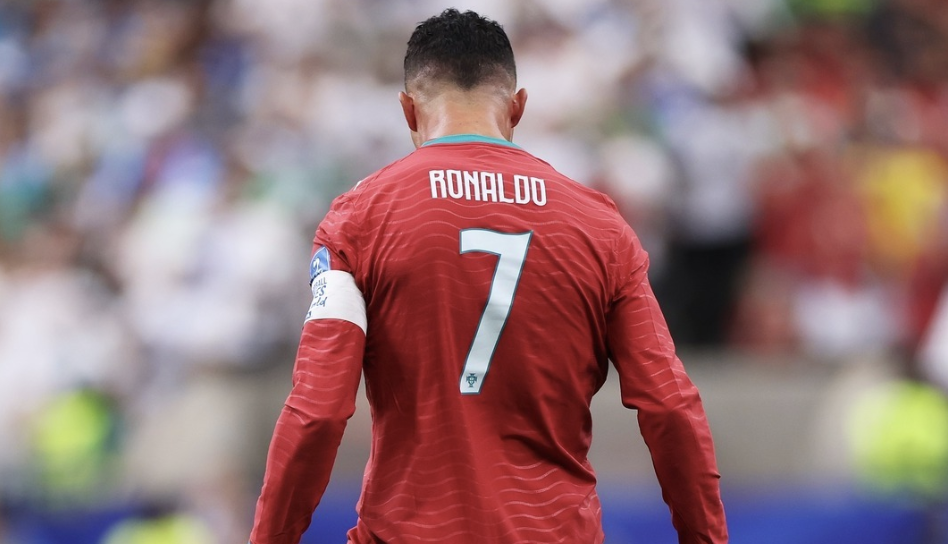 Cristiano Ronaldo from behind, wearing Portugal's red number 7 shirt, walking on the pitch with a packed stadium blurred in the background